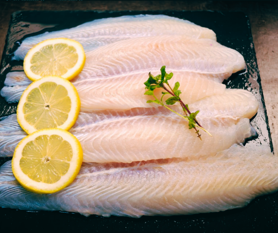 Silver Whiting fish fillets with lemon slices and herbs on a dark surface